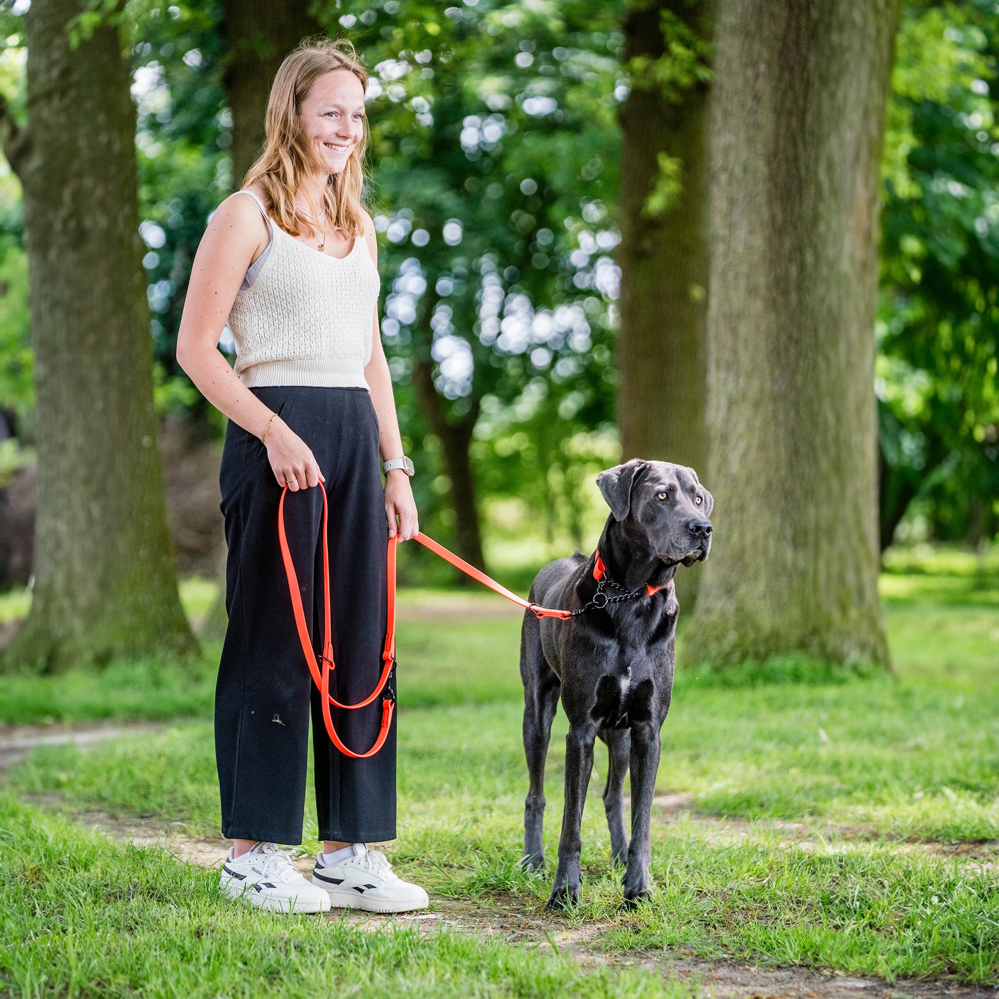 Frau und schwarzer Hund mit orangenen Biothane Halsband und orangener Biothane Leine im Park