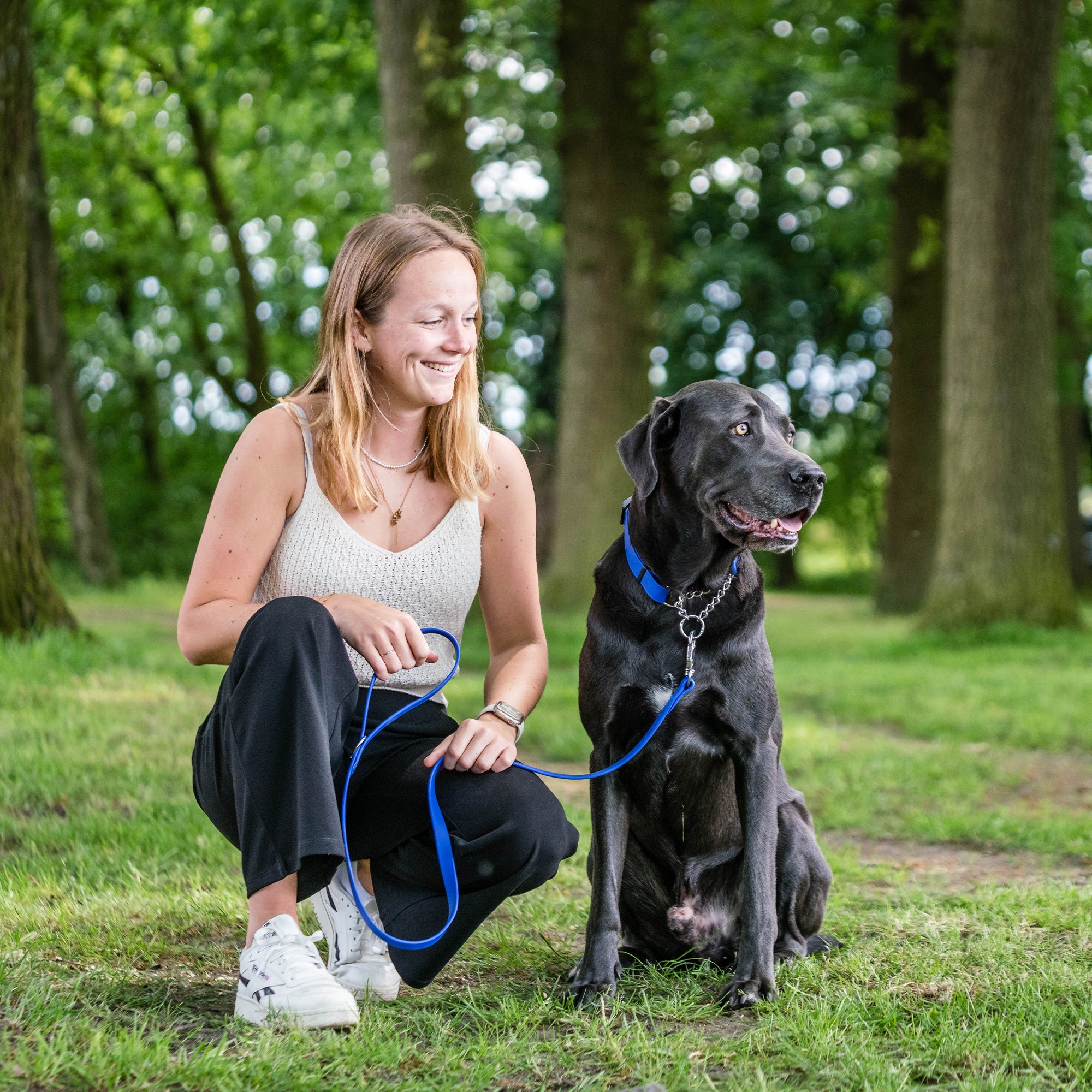 Frau und schwarzer Hund mit blauen Biothane Halsband und blauer Biothane Hundeleine im Wald