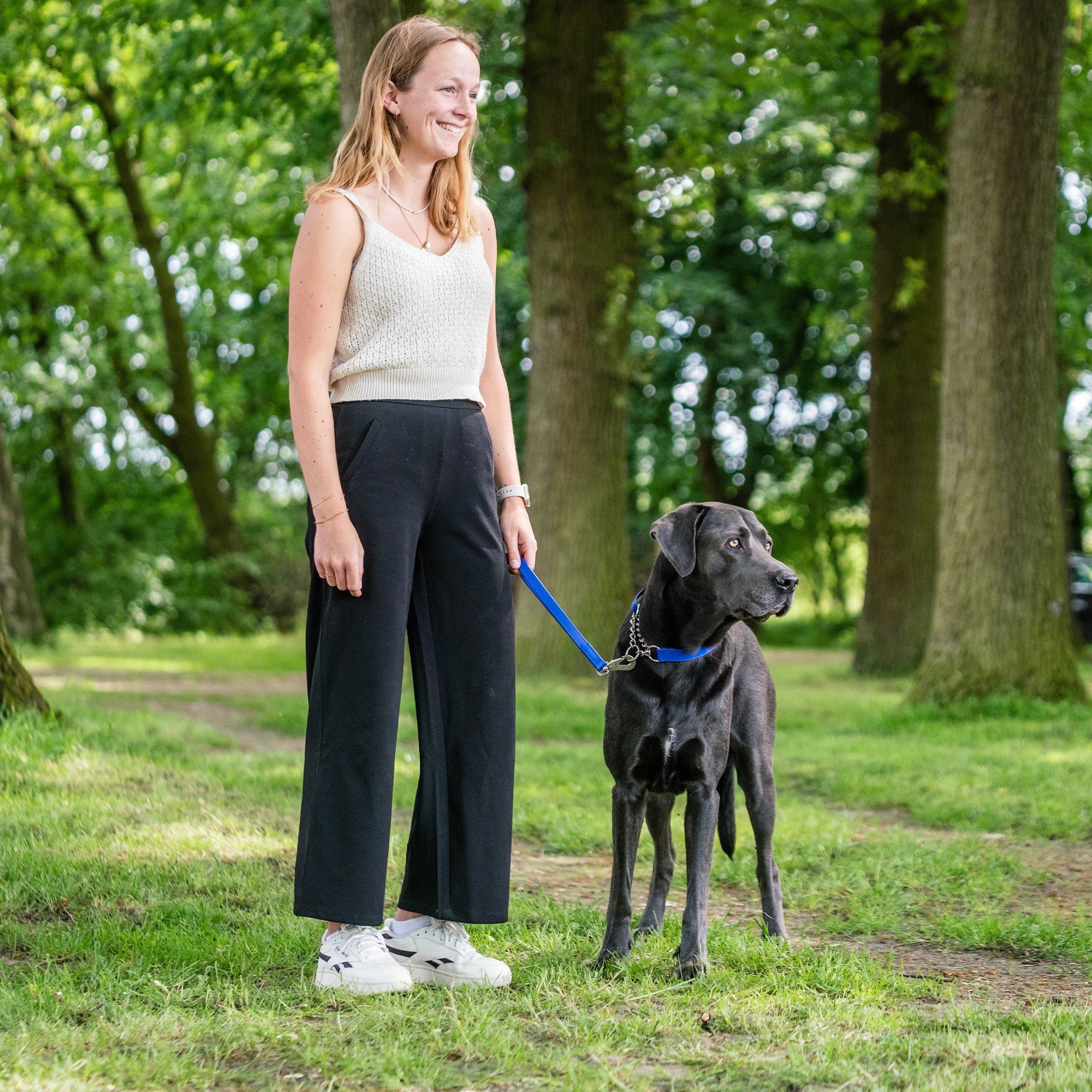 Frau und schwarzer Hund mit blauen Biothane Halsband und blauen Biothane Kurzführer im Park