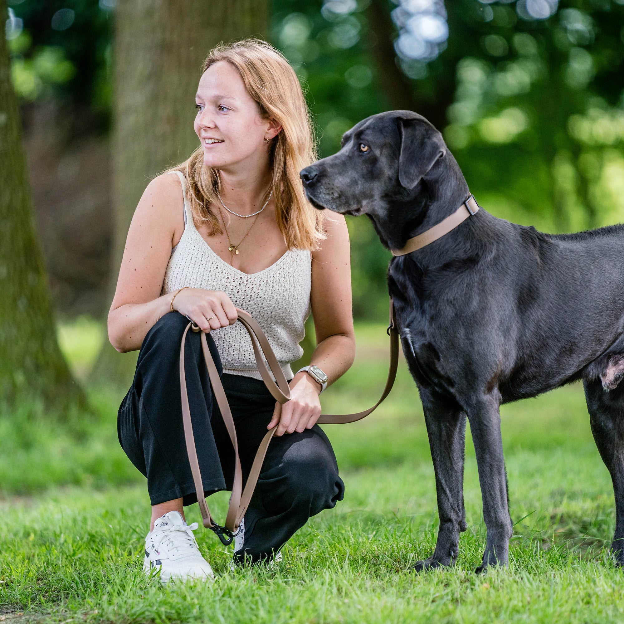 Frau undschwarzer Hund mit braunen Biothane Halsband an brauner Biothane Leine auf einer Wiese